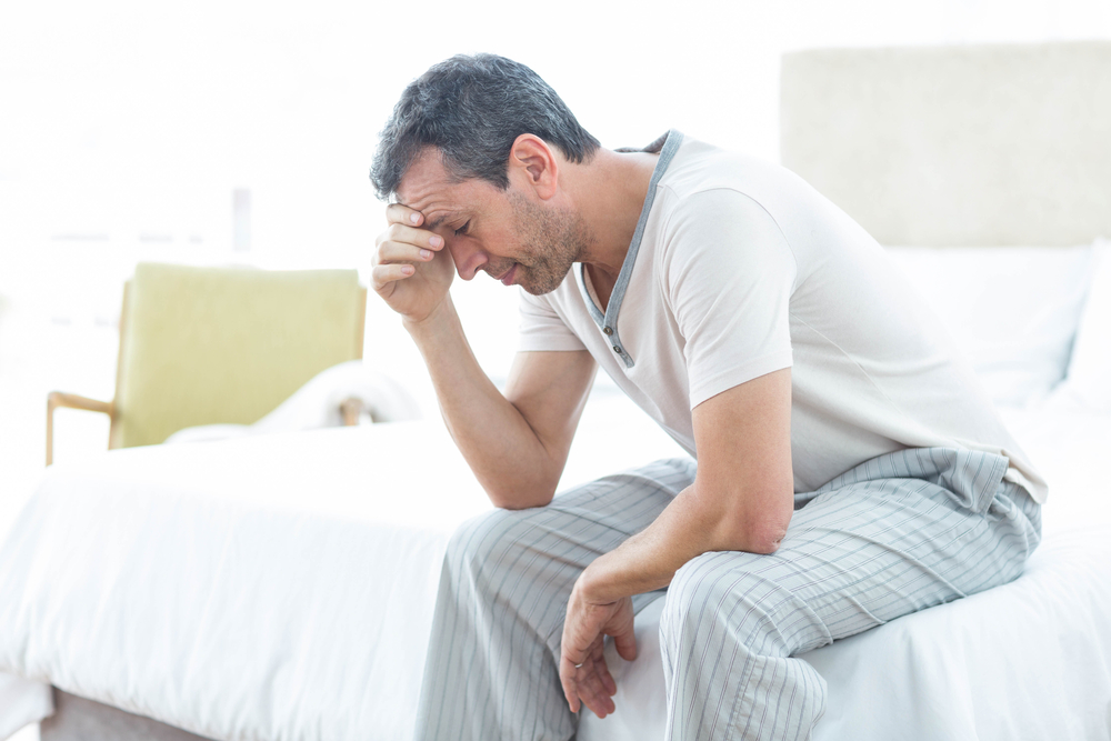 concerned man sitting at the end of his bed with hand on head